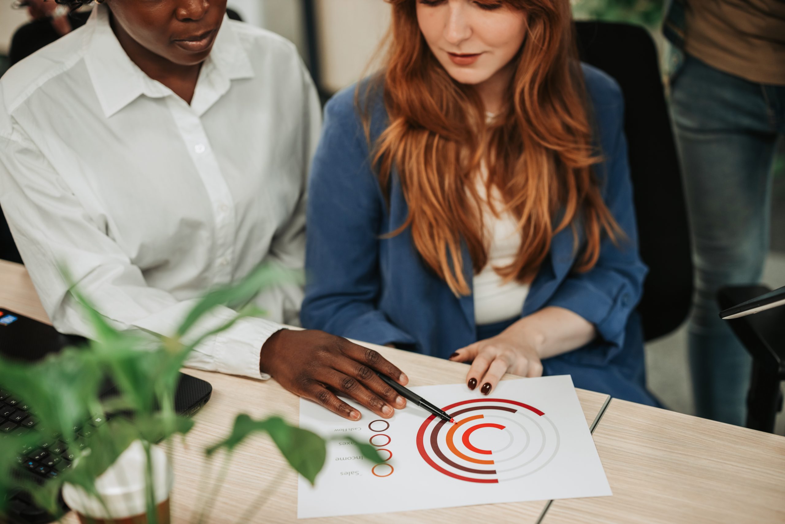 Multiracial colleagues working on their project and looking at documents in an office. Business professionals meeting in office. Focus on a diverse woman hands pointing on charts on a desk.